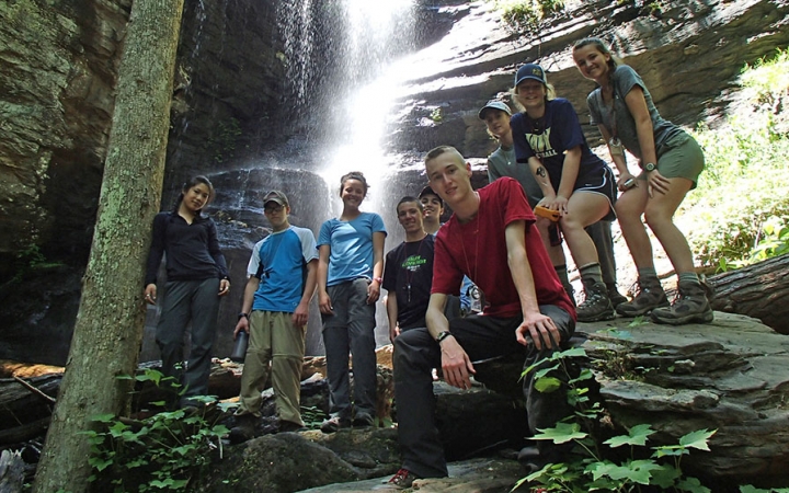 A group of students pose for a photo in front of a waterfall. 
